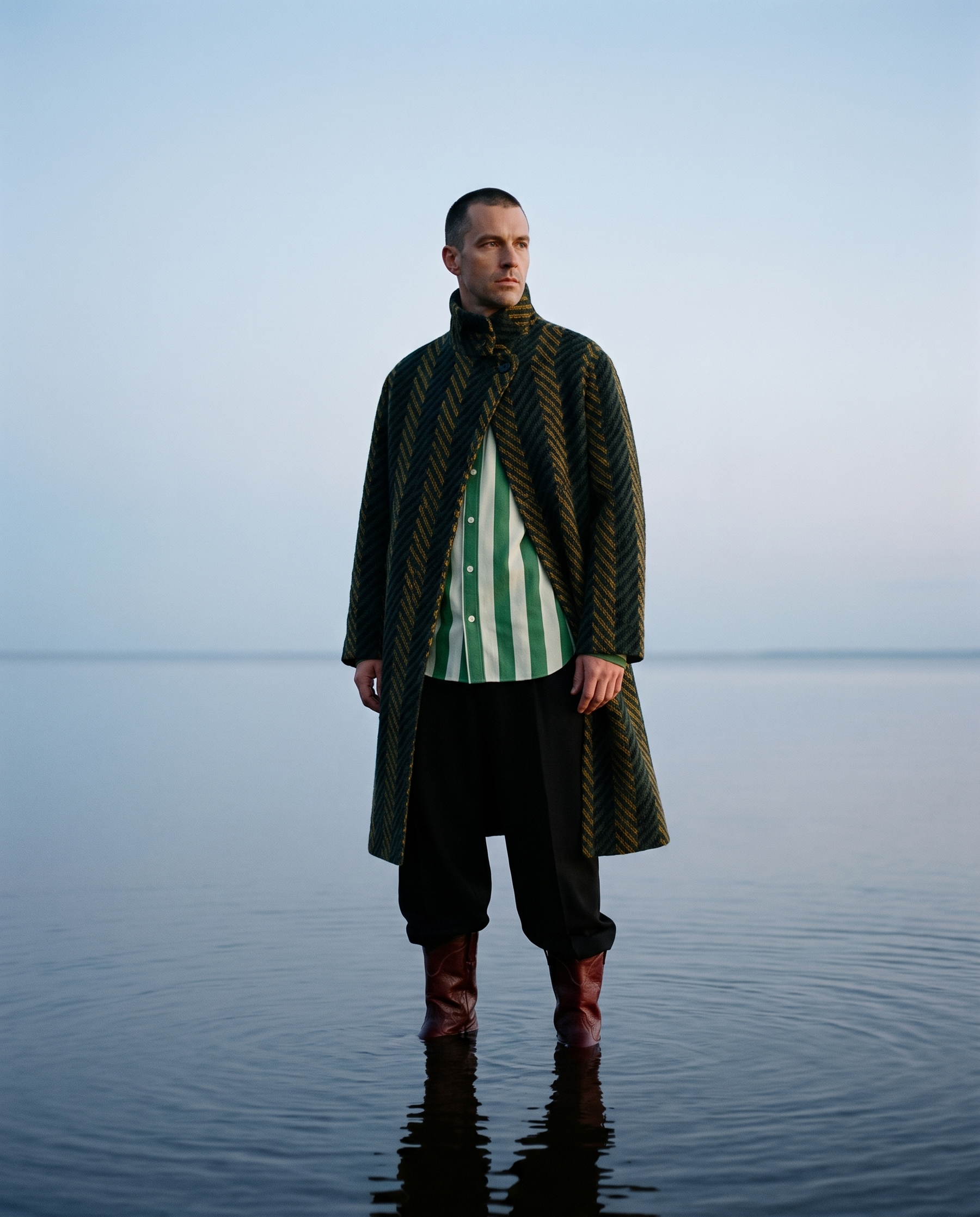 Model wearing a green-and-white striped shirt beneath a dark jacket.